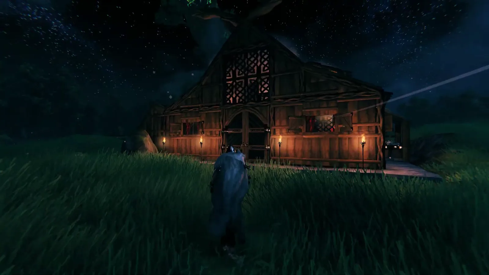 A timber Viking longhouse illuminated by torches beneath a starry sky